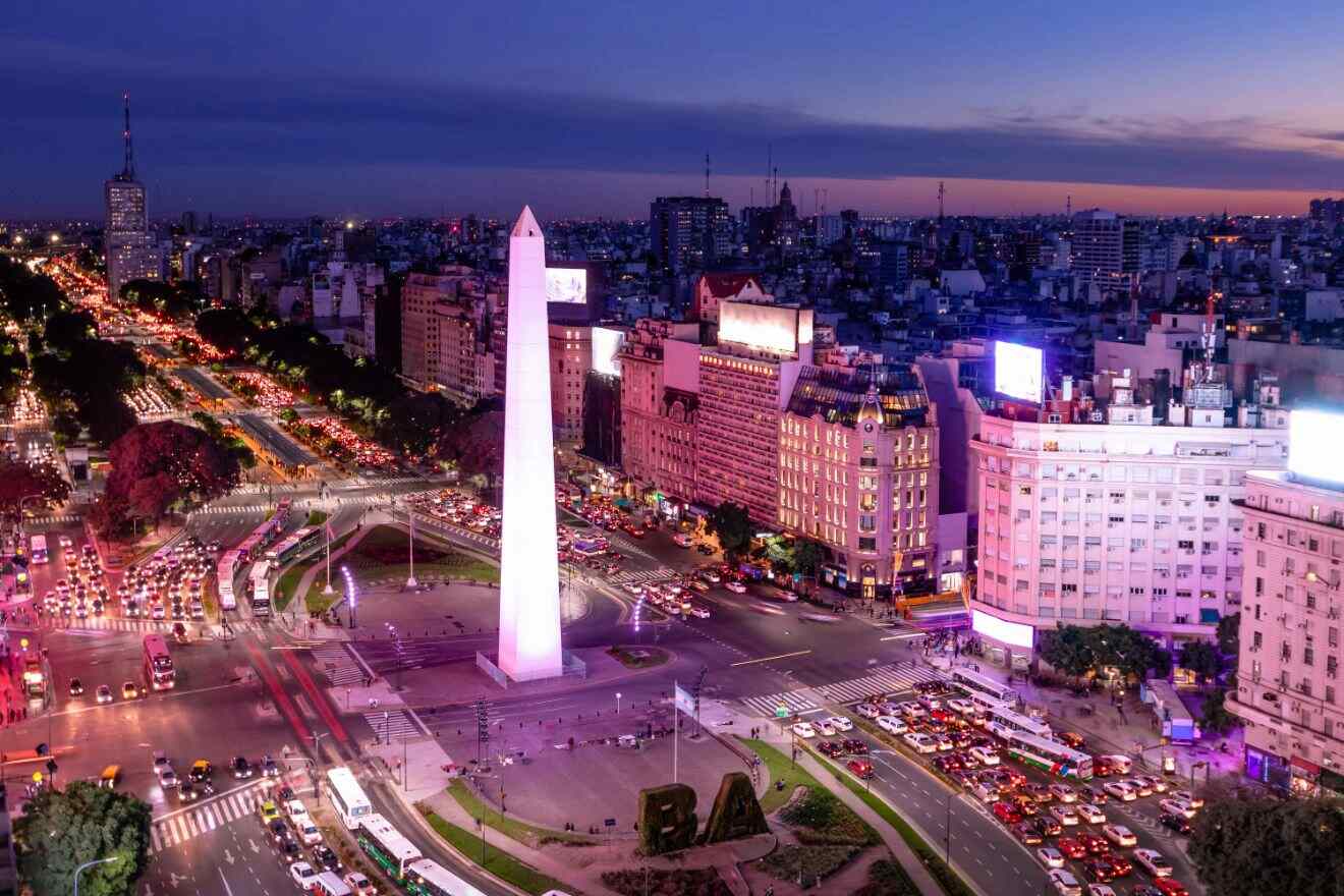 A breathtaking aerial night view of Buenos Aires, highlighting the iconic Obelisco de Buenos Aires, bathed in purple light, with busy traffic and city lights stretching into the horizon