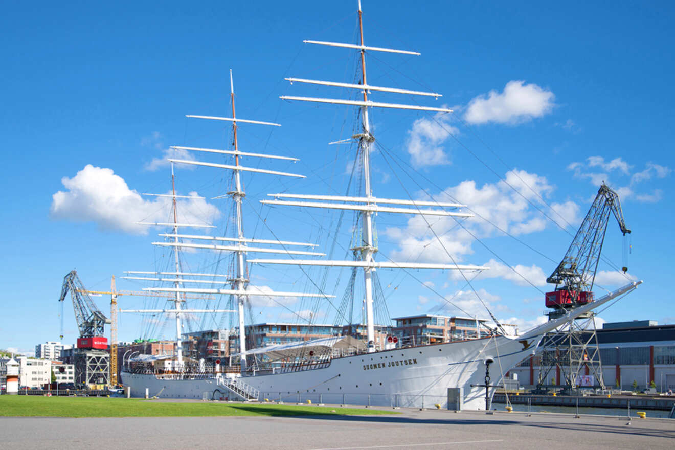 The majestic white sails of the 'Suomen Joutsen' ship at Forum Marinum, with blue skies and crane structures in the backdrop in Turku's maritime museum