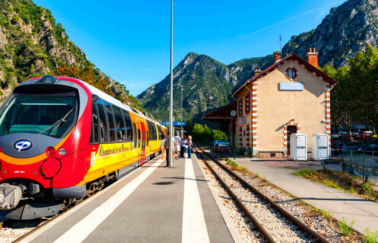 Vibrant red and yellow train at La Vésubie station with passengers, set against a backdrop of the Southern France mountains