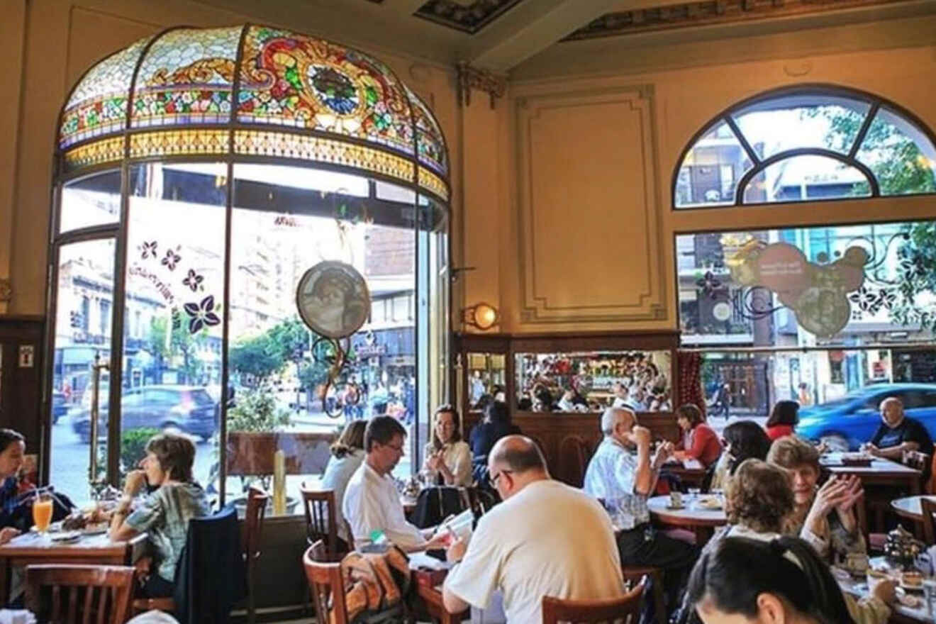 The classic interior of Confitería Las Violetas in Buenos Aires, with patrons enjoying the café's offerings under an ornate stained-glass window