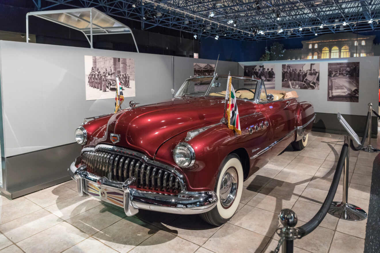 A classic red convertible car displayed at the Royal Automobile Museum in Amman, Jordan, with historical photos in the background