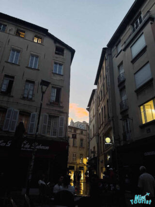 An evening scene in a bustling street of the South of France, with warm lights illuminating the facades of buildings and locals enjoying the atmosphere