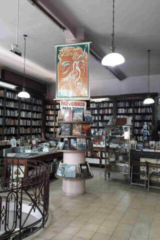 Interior of the oldest bookstore in Argentina, Buenos Aires, featuring high shelves lined with books, a central spiral staircase, and a vintage banner reading 'Paz y Libros para Todos' hanging from the ceiling