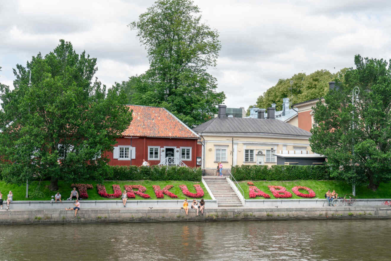 Charming view of the Turku riverside, featuring the historic Pharmacy Museum and the Qwensel House with lush greenery and people enjoying the riverbank
