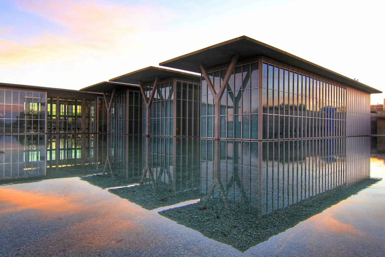 Modern architectural design of a glass building reflecting the sky and surrounded by still water, showcasing mid-century modern aesthetics in the Cultural District of Forth Worth.