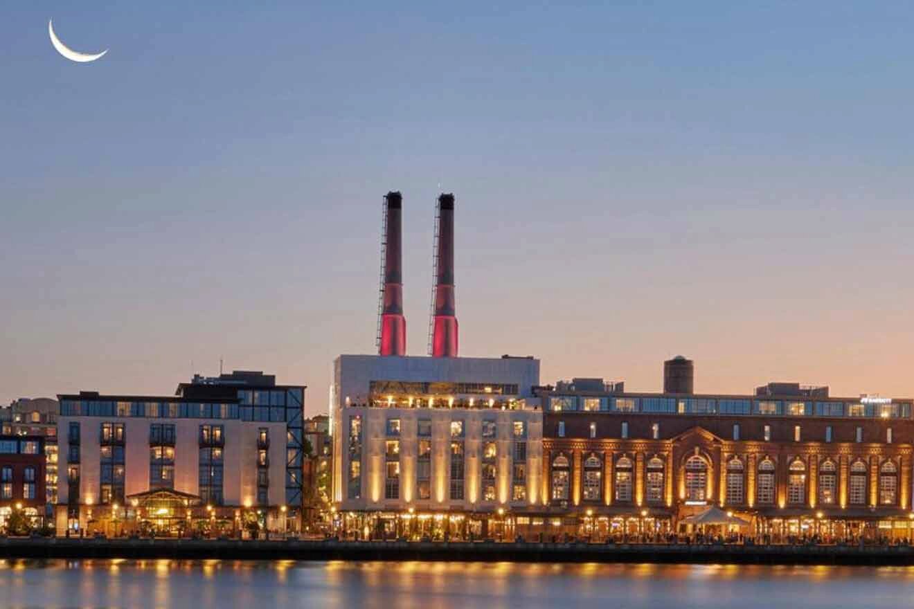The Riverside District in Savannah at dusk, with the historic power plant's iconic red stacks under a crescent moon.