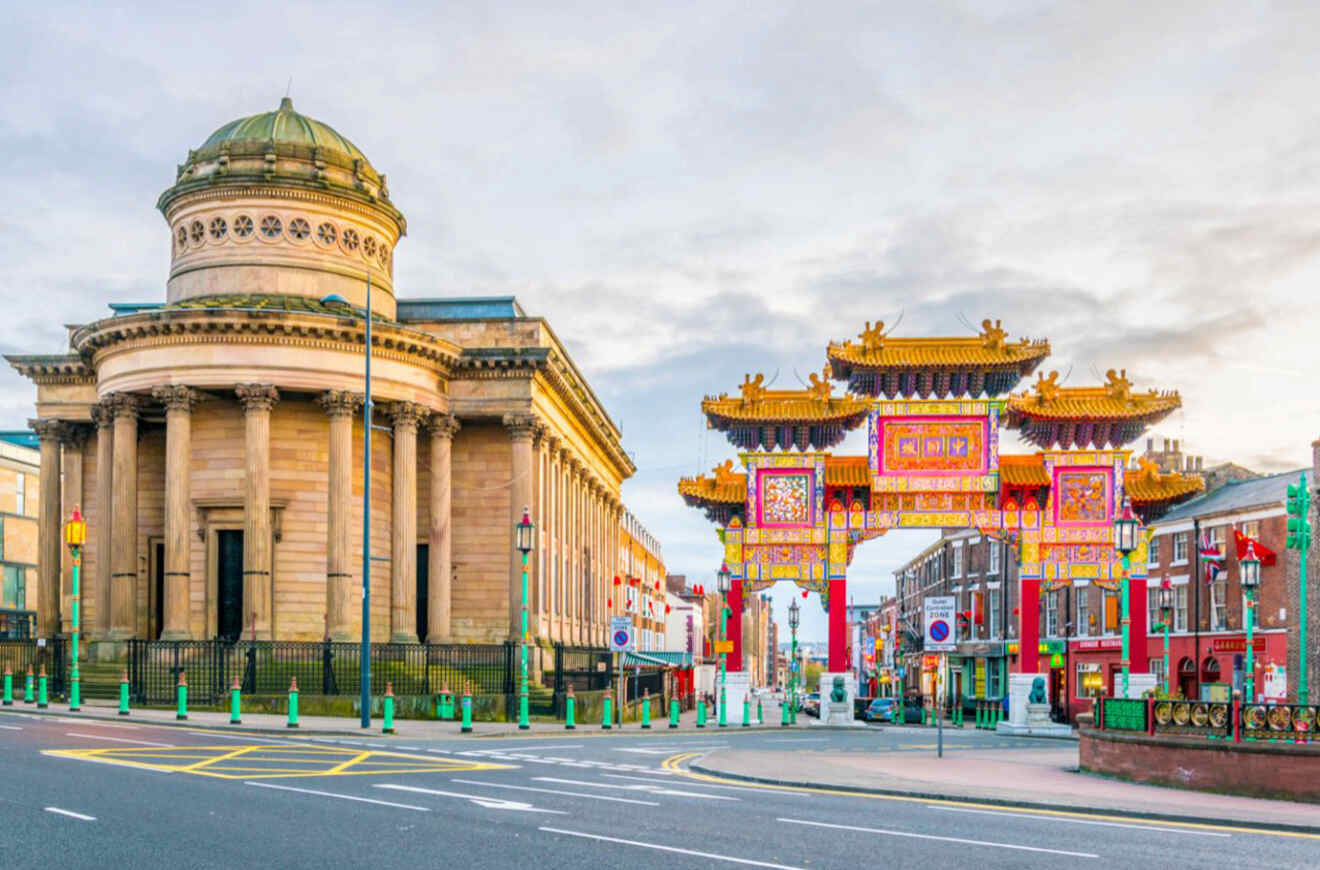 The striking traditional Chinese architecture of Liverpool's Chinatown gateway, with the grandiose Liverpool Empire Theatre to the left, under a clear sky.