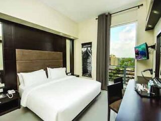 A modern hotel room with a large window, a flat-screen TV, and a work desk, offering a comfortable stay with a view.