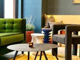 A cozy hotel sitting area with a bright green tufted sofa, dark armchairs, and eclectic decor elements creating a lively space.