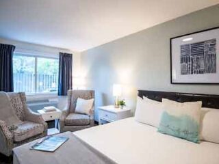 Neutral-toned hotel room with comfortable seating, a large bed with pillows, and an elegant wall art piece, providing a serene stay for guests.