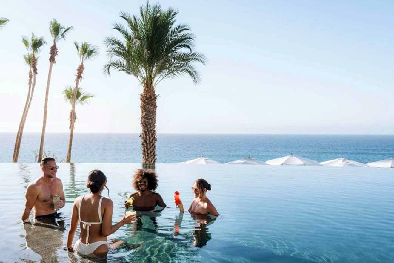 Infinity pool at a Cabo San Lucas hotel with guests enjoying drinks, flanked by tall palm trees, overlooking the tranquil sea blending with the horizon.