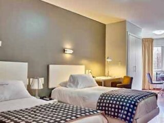A twin hotel room with chic décor, featuring checkered bedding and a comfortable seating area, exuding contemporary elegance.