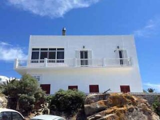 Traditional white Greek house with blue shutters and a clear sky above