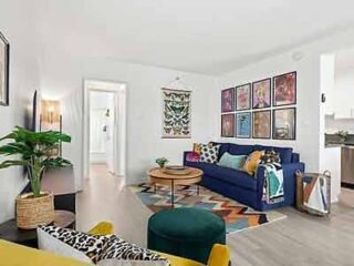 A vibrant living room with eclectic decor, including a blue sofa, patterned wall art, and a mix of colorful and textured furnishings.