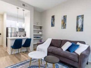 Modern apartment living area with a gray couch, blue accent chairs, and a chic white coffee table on a patterned rug, offering a sleek, contemporary vibe.