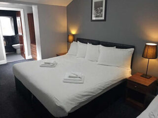 A neatly arranged hotel room with a large double bed, white bedding, and flanking nightstands with lamps, creating a comfortable and inviting atmosphere