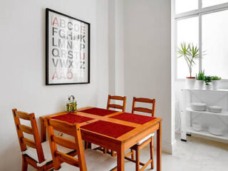 Simple dining space with a wooden table, chairs, and a framed alphabet poster on the wall, next to a bright window
