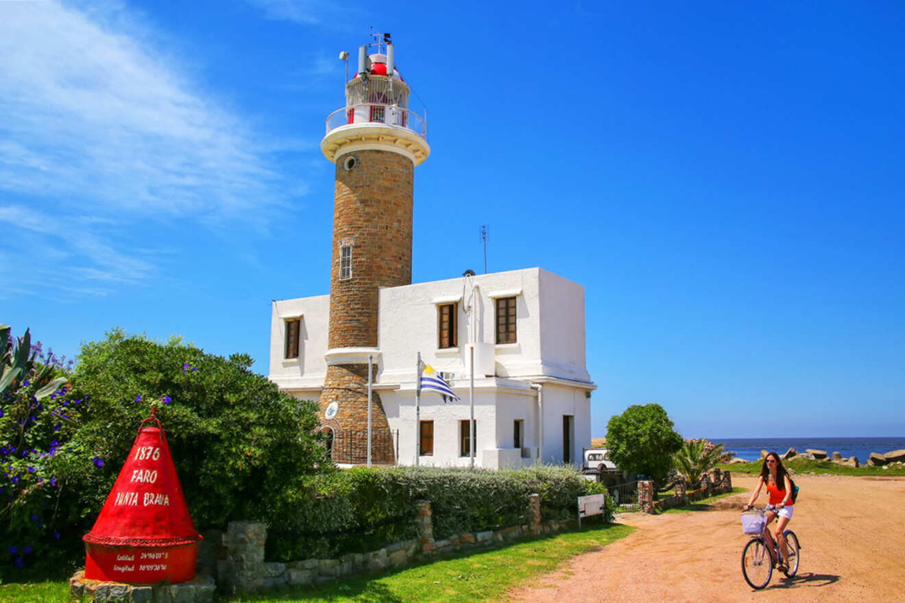 A woman enjoying a bicycle ride on a clear day near the historic Punta Brava Lighthouse in Uruguay, with a bright blue sky overhead and lush greenery surrounding the path.
