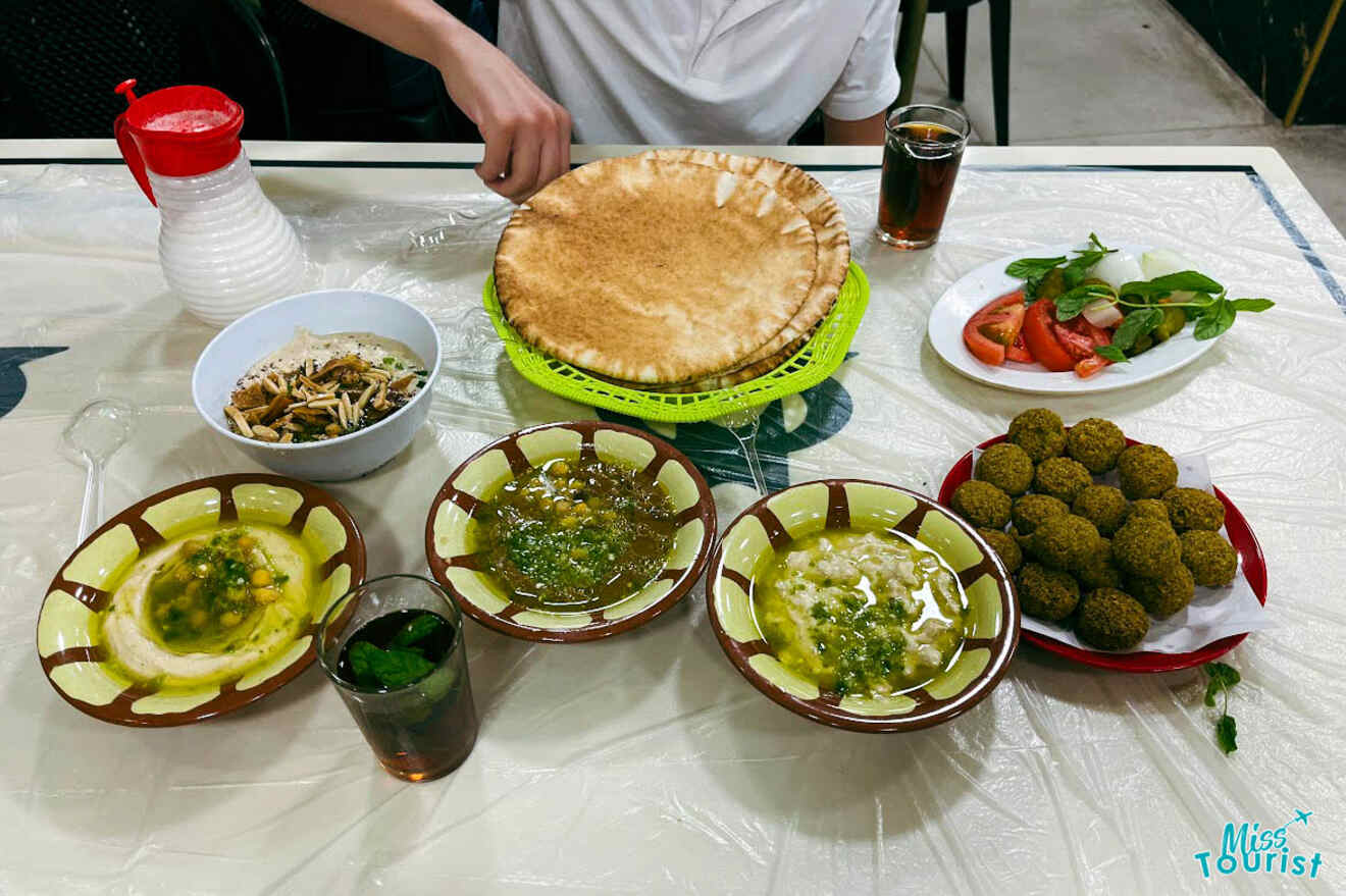 An overhead view of a traditional Jordanian meal with hummus, falafel, salads, and large flatbread, served on a plastic-covered table