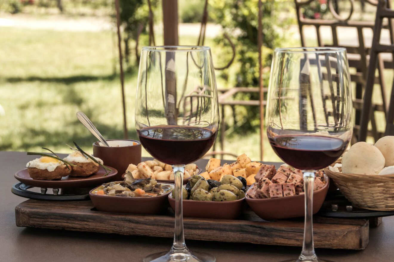 A cozy outdoor wine tasting setup featuring two glasses of red wine, assorted tapas on a wooden board, and a view of a vineyard in the background
