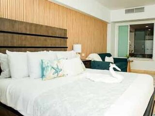 Hotel bedroom with a white bedspread, wooden headboard, and decorative pillows with a starfish and swan towel art.