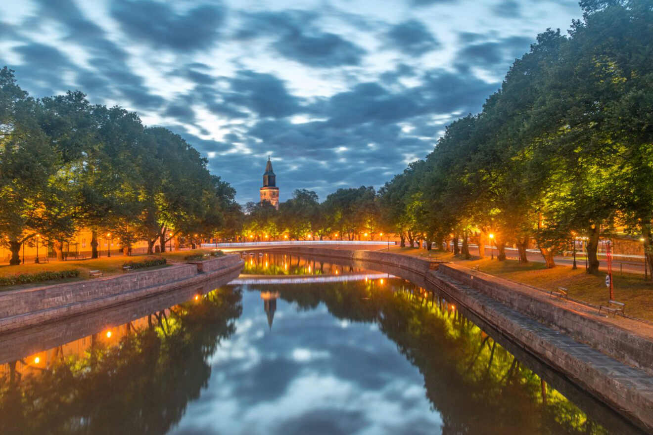 Riverside promenade in Turku during twilight with the illuminated façade of Turku Cathedral reflected in the still waters of Aura River, under a dramatic sky