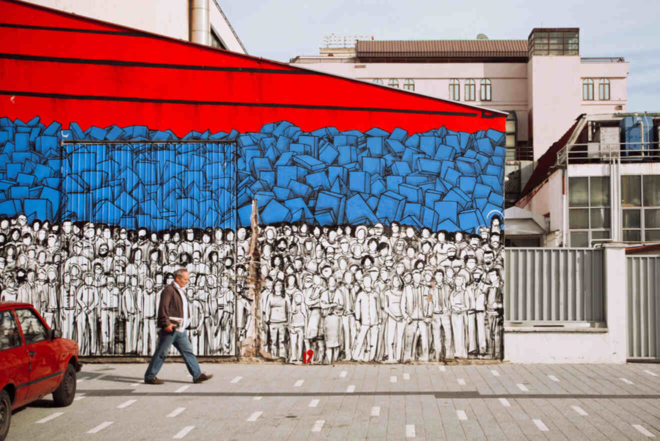 Vibrant street art mural in Belgrade depicting a crowd of people in black and white against a bright blue background of broken walls