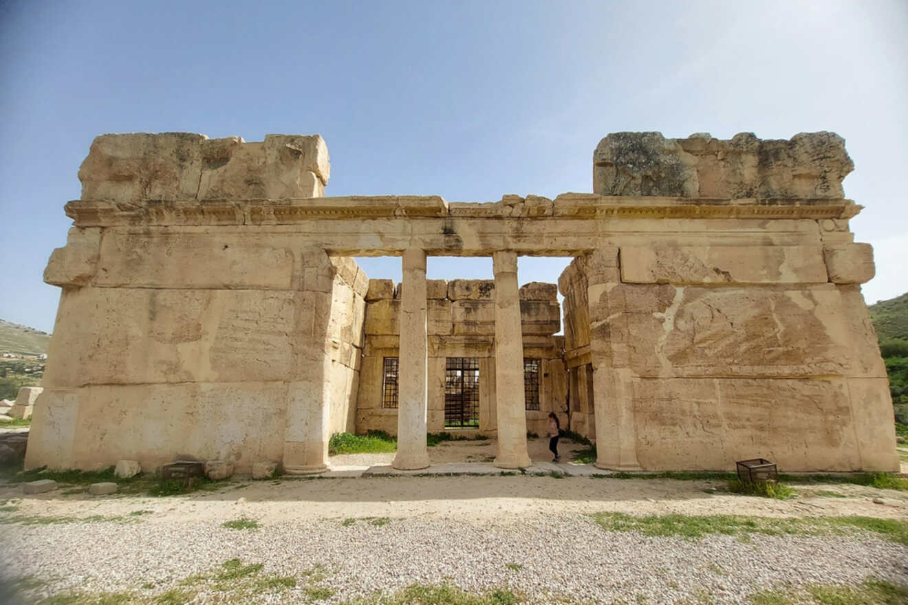 The ruins of Qasr Al-Abed, a large limestone structure with towering columns and carved doorways, standing under a clear sky in Amman, Jordan