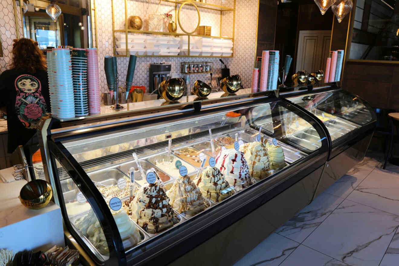 A cozy Tel Aviv ice cream shop with an elegant interior, showcasing a wide array of ice cream flavors in a glass display case and stacks of colorful cones