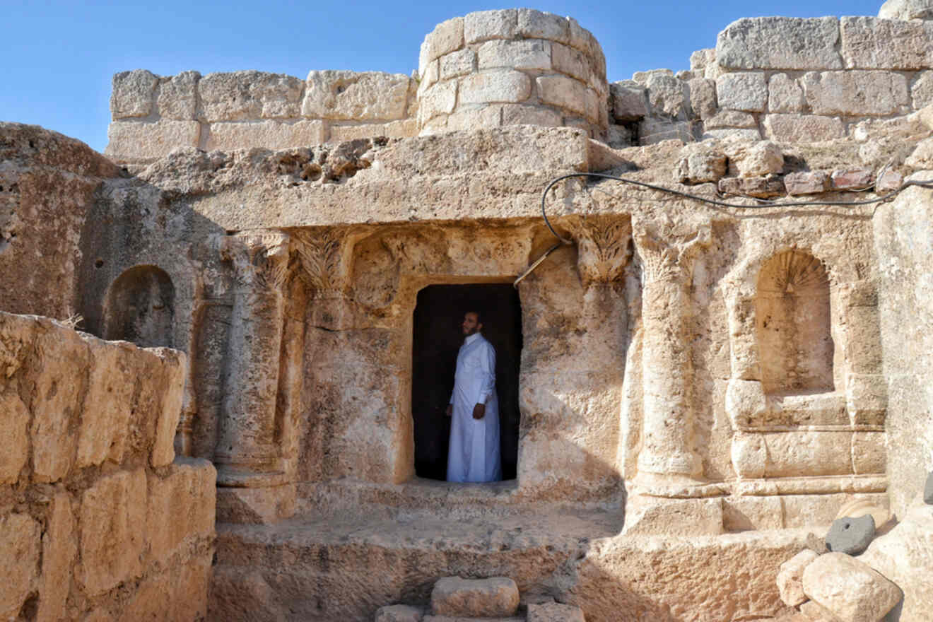 A man in traditional white attire standing in the doorway of an ancient stone cave at the historical site of the Cave of Seven Sleepers near Amman, Jordan