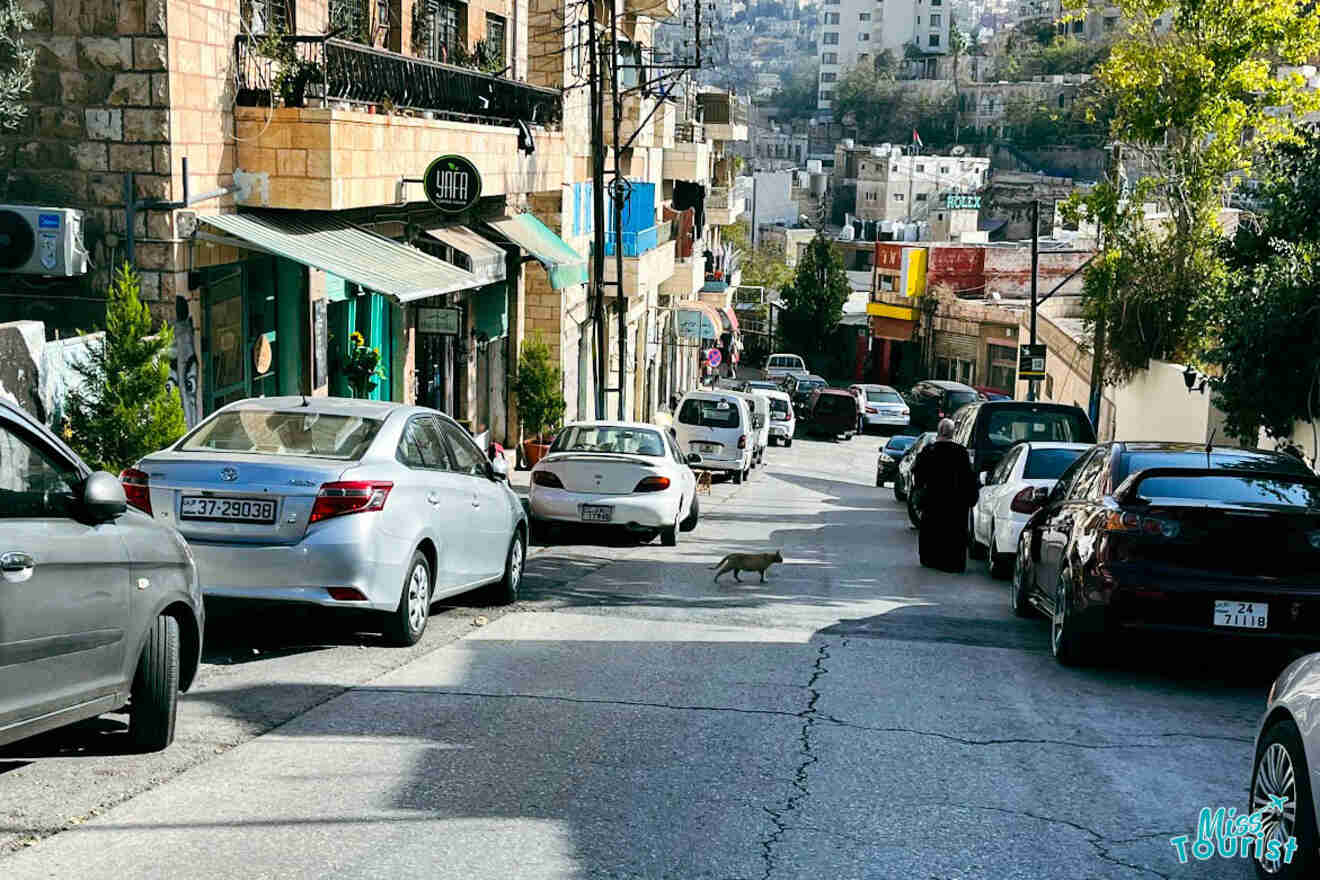 A typical street scene in Amman, Jordan, with cars parked along the road and a man walking