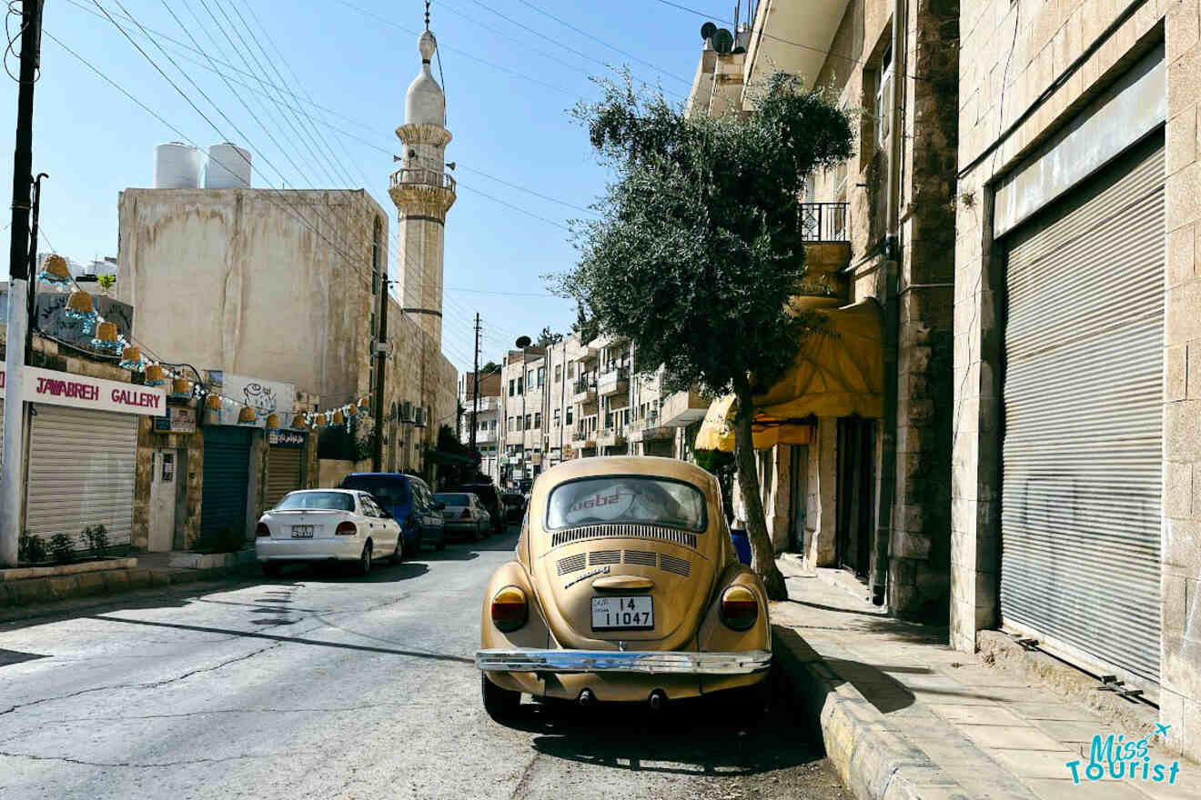 A classic Volkswagen Beetle parked on a street in Amman, Jordan, with the city's limestone buildings and a minaret in the background