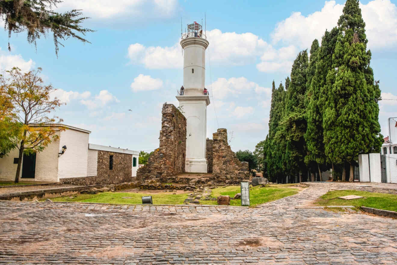 A view of the picturesque lighthouse amid the ruins in Colonia, Uruguay, a popular day trip destination from Buenos Aires, set against a cobblestone path and lush greenery