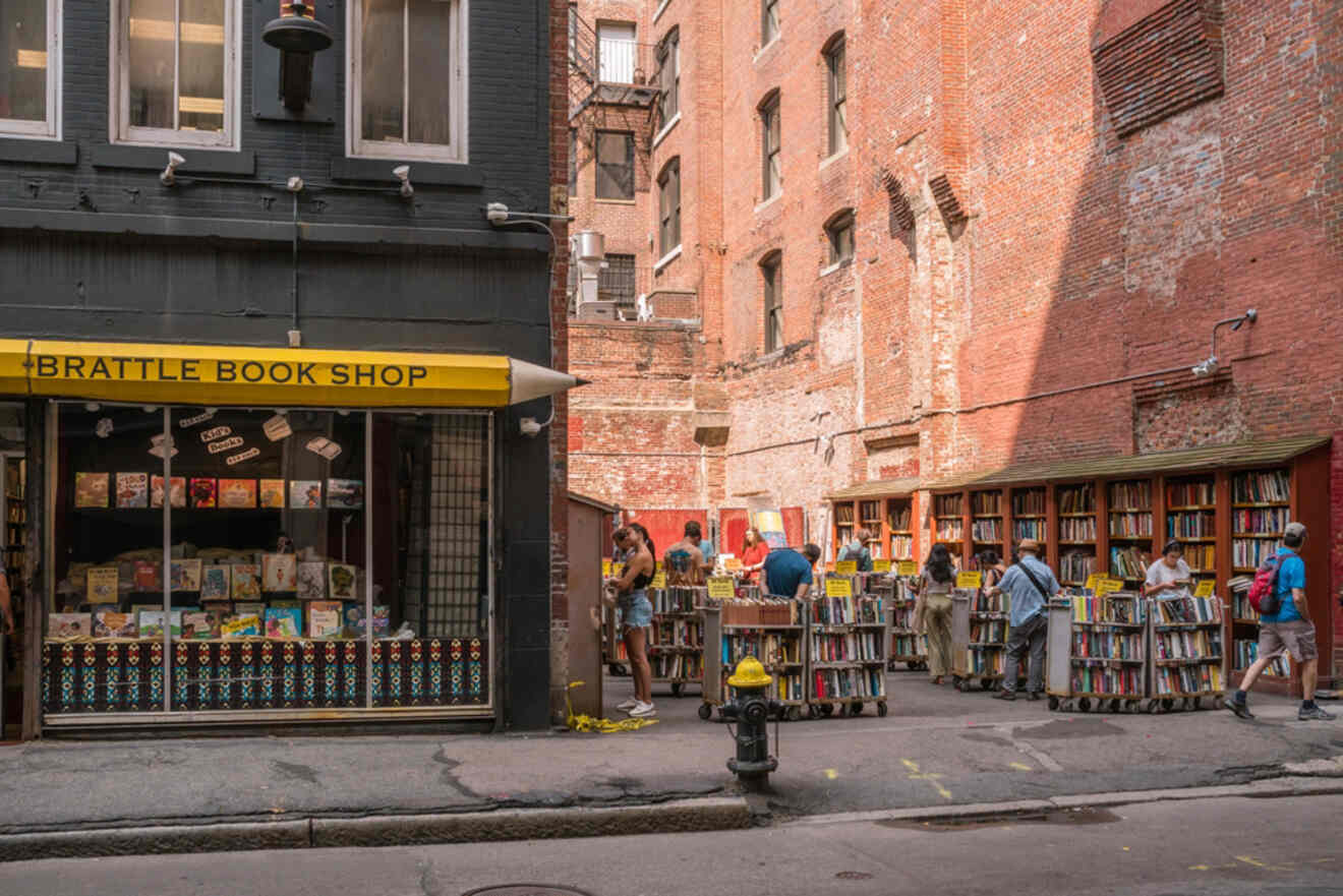 Customers browsing books at the outdoor stalls of Brattle Book Shop, an iconic bookstore in Boston, with red awnings and a historic brick building backdrop