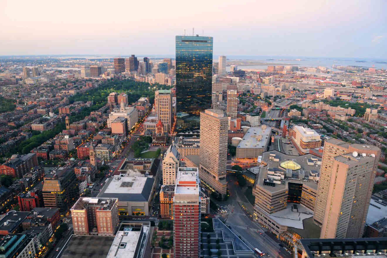 Panoramic cityscape of Boston at dusk, featuring the John Hancock Tower and Prudential Center against the twilight sky, as seen from a high vantage point