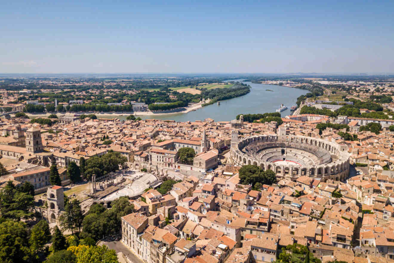 Aerial view of Arles, France, showcasing the historic Roman amphitheater surrounded by dense urban buildings and the Rhone River in the background