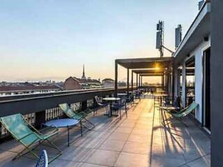 A rooftop terrace at dusk with loungers and tables set against a backdrop of cityscape and sunset, reflecting a serene urban evening ambiance.
