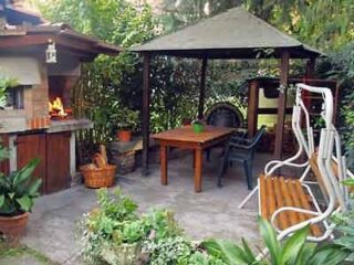 An outdoor patio area with a sheltered dining space, brick BBQ setup, and comfortable seating surrounded by lush potted plants for a homely garden ambiance.
