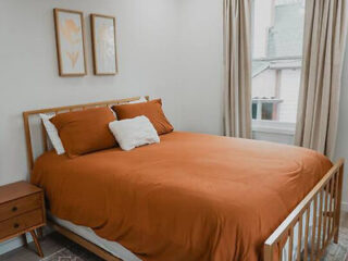 Simple and neat bedroom with an orange duvet, white pillows, and minimalist wall art