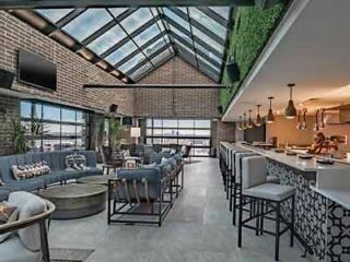 An industrial-chic hotel bar with a glass ceiling, brick walls, and a green living wall, offering a trendy space for guests to unwind.