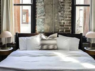 Luxurious and minimalist bedroom setup in The Grant by Black Swan, showcasing comfort and style with exposed brickwork and elegant bedside lamps.