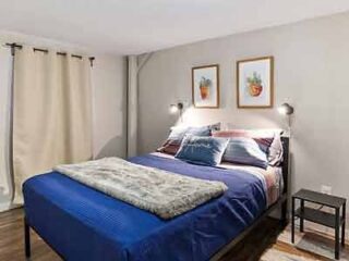 A cozy bedroom with blue bedding, framed botanical prints, and warm lighting, providing a comfortable and inviting atmosphere.