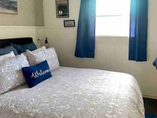 Bedroom with a white lace-patterned comforter, personalized with a navy blue pillow, accented by matching curtains for a personalized touch.