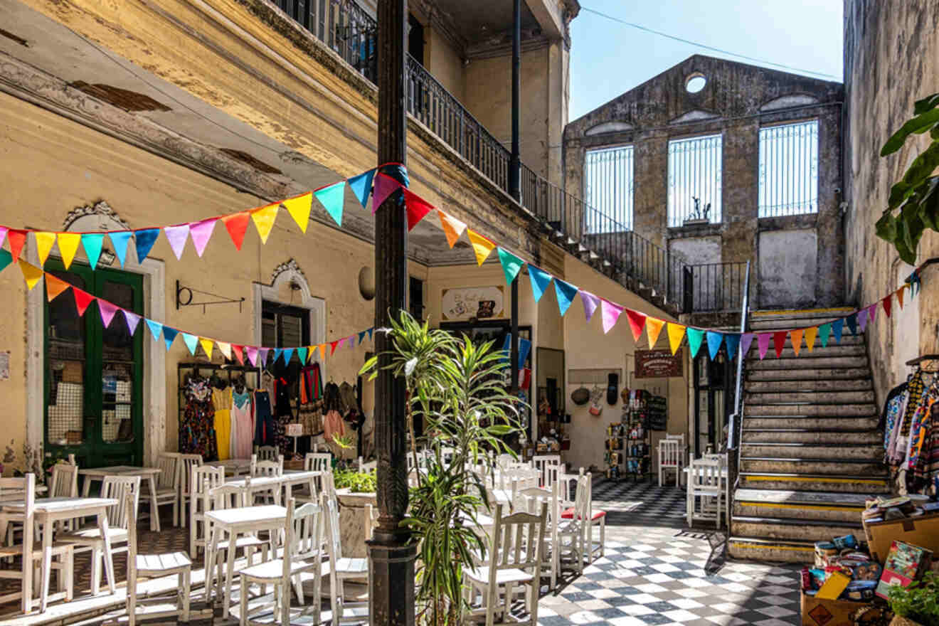 The vibrant and historical Pasaje Defensa in San Telmo, Buenos Aires, adorned with colorful flags, showcasing outdoor white dining tables against a backdrop of classic architecture and eclectic local shops