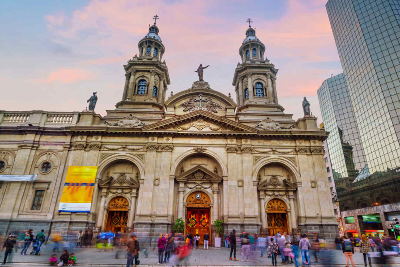 Close-up view of the ornate façade of the Santiago Metropolitan Cathedral with people blurred in motion, set against modern skyscrapers during twiligh