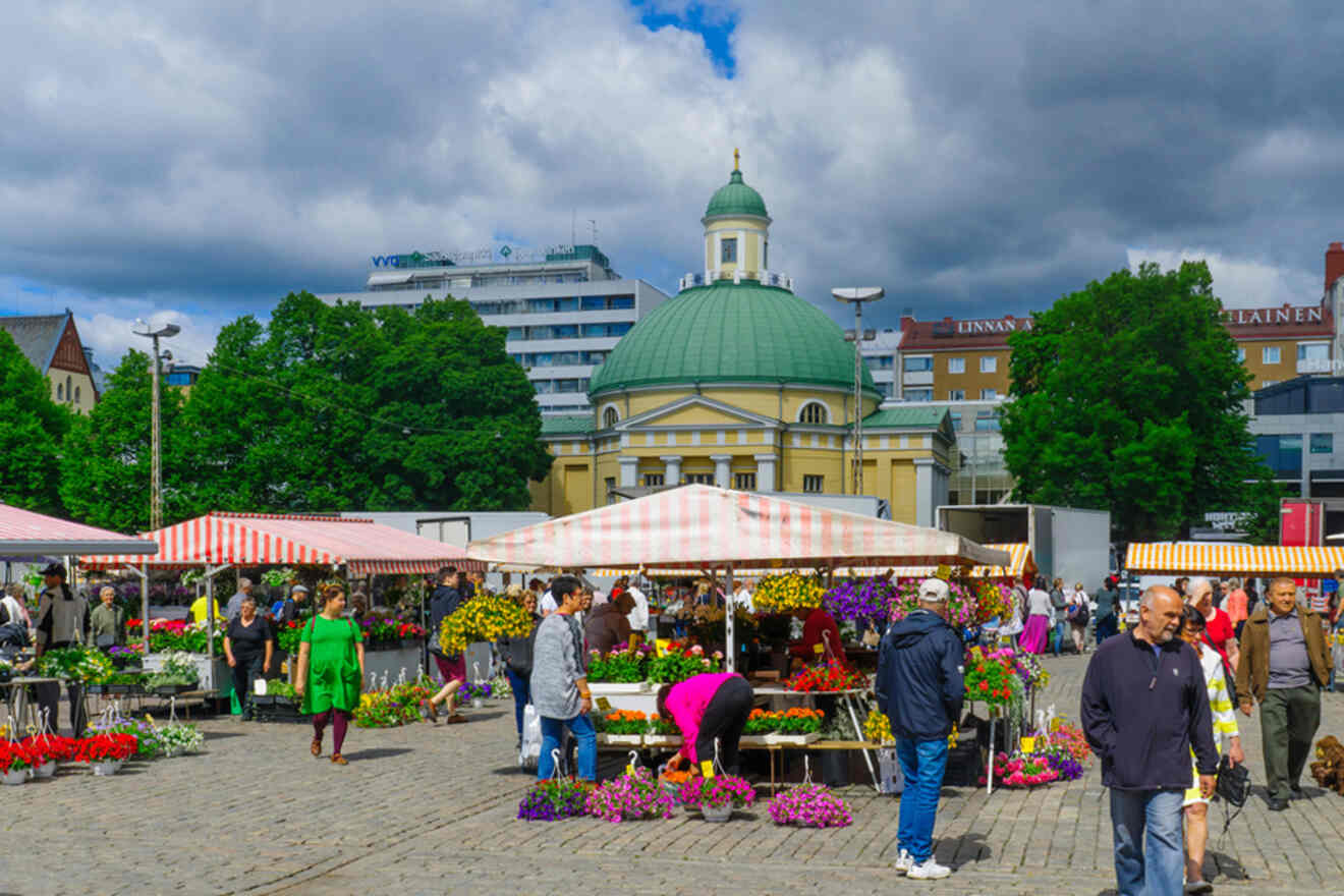 Vibrant Turku Market Square bustling with people shopping for flowers and produce, with the classical architecture of the Old Great Square in the background