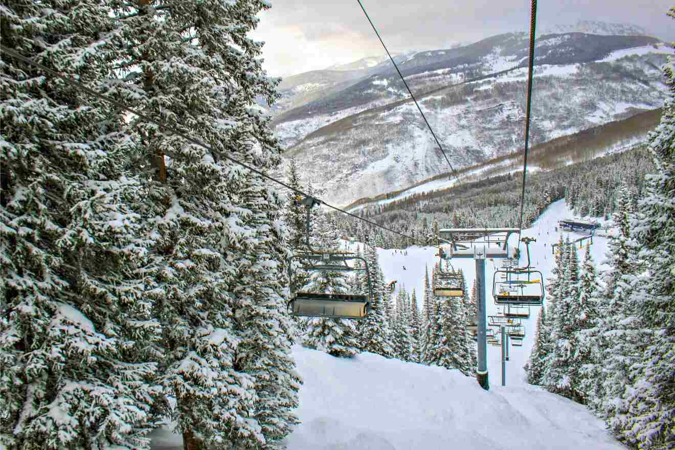Ski lift in Vail, Colorado carrying bundled-up skiers through a snowy forest with a view of distant mountains and ski trails