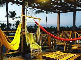 Rustic outdoor lounge area with wooden furniture and hammocks at Hostel Eco Punta Cana, set against a twilight sky.