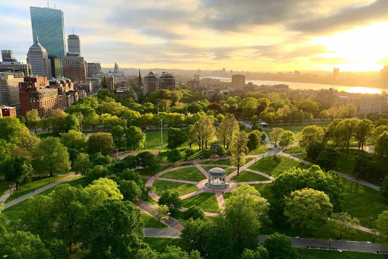 Sunset view of the Boston Public Garden with its lush greenery, walking paths, and the famous gazebo, with the city skyline in soft evening light