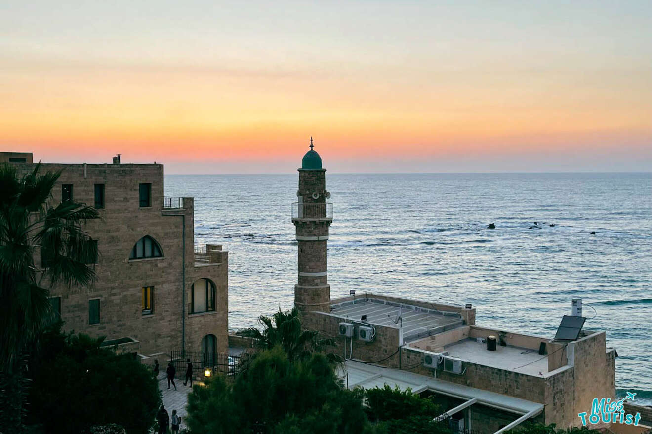 A serene sunset view at the Tel Aviv coastline with the silhouette of an old mosque and buildings overlooking the calm Mediterranean Sea